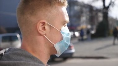 Tıbbi maskeli genç adam profili şehir caddesinde yürüyor. Dışarıdaki kalabalığın içinde virüsten koruyucu maske takan adam. Koronavirüs ve salgın hastalıklardan korunan sağlık ve güvenlik kavramı