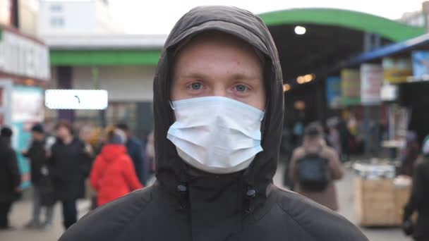 Porträtt av ung man med medicinsk ansiktsmask står på stadens gata. Killen bär skyddsmask från virus utomhus i folket trängsel. Begreppet hälsa och säkerhet liv från coronavirus pandemi — Stockvideo