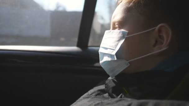 Niño pequeño con mascarilla médica viajando en coche y mirando por la ventana. El niño triste usa una máscara protectora del virus durante el viaje. Concepto de salud y seguridad de la pandemia de coronavirus — Vídeos de Stock