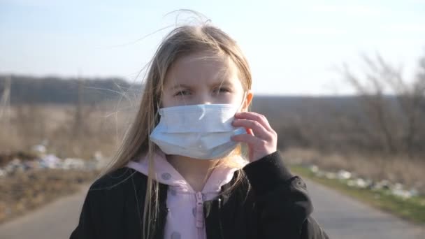 Портрет маленької дівчинки з маскою для обличчя, що стоїть на відкритому повітрі. Щаслива дитина знімає захисну маску від вірусу та посміхається. Концепція здоров'я та безпеки життя від коронавірусу та пандемії — стокове відео