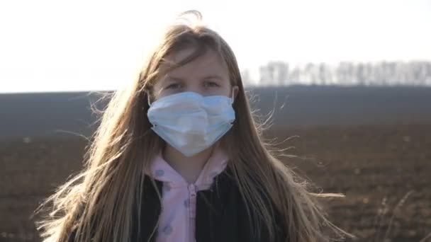 Retrato de menina com máscara facial médica em pé ao ar livre. Criança triste usando máscara protetora do vírus lá fora. Conceito de saúde e segurança vida de coronavírus e pandemia. Fechar — Vídeo de Stock