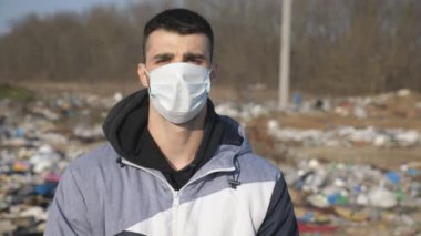Dışarıdaki virüsten koruyucu maske takan adam. Tıbbi maskeli genç bir adamın portresi doğada duruyor. Koronavirüs ve salgın hastalıklardan korunan sağlık ve güvenlik kavramı. Kapat.