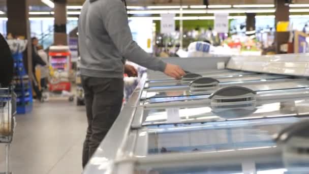 Mann mit medizinischer Gesichtsmaske öffnet Glastür in Kühlabteilung im Supermarkt und wählt gekühlte Lebensmittel. Junger Mann nimmt Produkt aus Kühlschrank im Geschäft. Einkaufen während der Coronavirus-Pandemie — Stockvideo