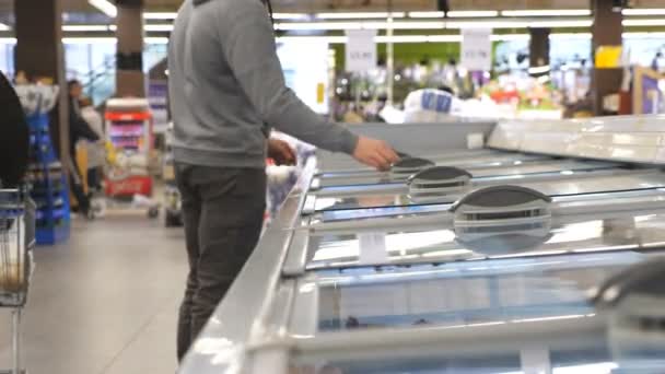 Man met medisch gezichtsmasker open glazen deur in gekoelde sectie bij supermarkt en kies gekoelde boodschappen. Jongeman die producten uit de koelkast haalt in de winkel. Winkelen tijdens een coronaviruspandemie — Stockvideo