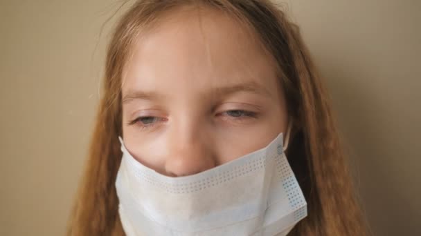 Πορτρέτο του μικρού κοριτσιού με ιατρική μάσκα προσώπου κατά τη διάρκεια της απομόνωσης. Θλιβερό θηλυκό παιδί φοράει προστατευτική μάσκα από ιό σε εσωτερικούς χώρους. Έννοια της ζωής για την υγεία και την ασφάλεια από το coronavirus και πανδημία. Κλείσε. — Αρχείο Βίντεο