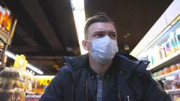 Ritratto di giovane uomo con maschera medica che cammina al supermercato. Un tizio che va al negozio con una maschera protettiva dal virus. Shopping in drogheria durante la pandemia di coronavirus. Concetto di salute. COVID-19 — Video Stock