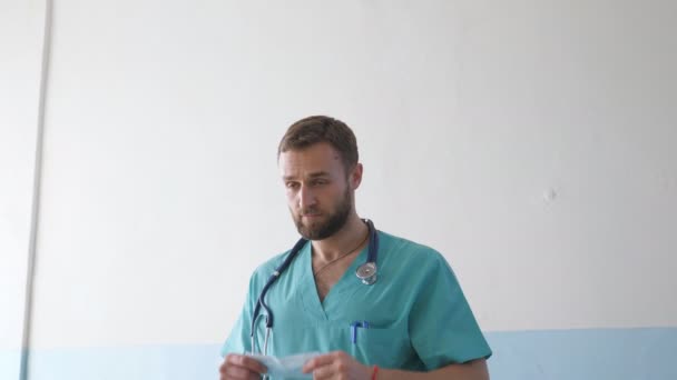 Ritratto di giovane medico caucasico maschio con maschera medica guarda la macchina fotografica. Operatore medico con maschera protettiva dal virus. Concetto di salute e sicurezza vita da pandemia di coronavirus. COVID-19 — Video Stock