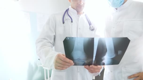 Medical workers in hospital examine x-ray prints. Male medics consult with each other while looking at x ray image. Two caucasian doctors view mri picture and discussing about it. Close up — Stock Video