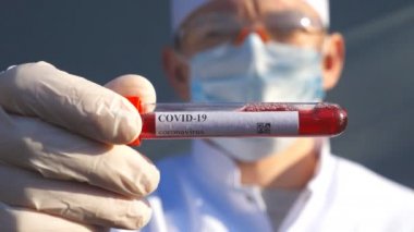 Doktor, Coronavirus 'a kan örneği veren bir test tüpü tutuyor. Koruyucu eldivenli sıhhiyenin eli laboratuarda kan örneklerini test ediyor. COVID-19 salgınından sağIık ve güvenlik kavramı. Kapat.