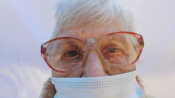 Portret van oma met een beschermend masker van het virus. Oudere dame die in de camera kijkt en droevige emoties toont. Concept van gezondheid en veiligheid als gevolg van een pandemie. Quarantaine van het coronavirus voor ouderen — Stockvideo