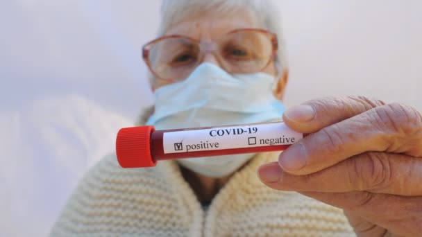 Vecchia signora con maschera protettiva che tiene il suo esame del sangue con esito positivo sul coronavirus. Malato nonna guardando in macchina fotografica mostrando emozioni tristi. Concetto di salute e sicurezza vita da pandemia COVID-19 — Video Stock