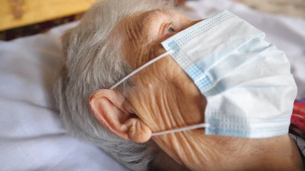 할머니가 바이러스로부터 마스크를 병원에서 침대에 동안무엇인가를 조사하는 시각을 코로나 바이러스로부터의 — 스톡 사진