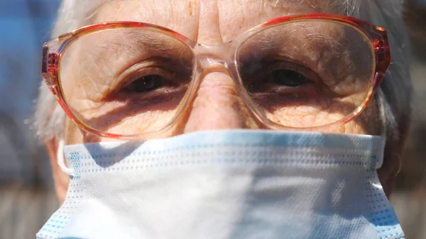 Detail portrait of granny in protective mask from virus. Elderly woman looking into camera with pensive sight. Concept of health and safety life from pandemic. Quarantine of coronavirus for old people.