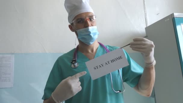 El doctor tiene una foto con la inscripción en casa durante la epidemia de coronavirus. Médico muestra cartel con un llamamiento al autoaislamiento. Concepto de vida en salud y seguridad de la pandemia de COVID-19 — Vídeo de stock