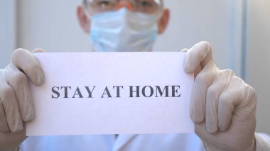 Sıhhiyeci kendini izole etmeye meyilli bir poster gösteriyor. Erkek doktor, Coronavirus salgını sırasında evde duran bir resim tutuyor. COVID-19 salgınından korunma kavramı
