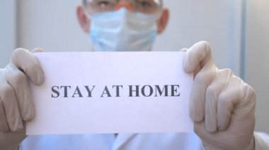 Sıhhiyeci kendini izole etmeye meyilli bir poster gösteriyor. Erkek doktor, Coronavirus salgını sırasında evde duran bir resim tutuyor. COVID-19 salgınından korunma kavramı