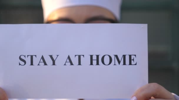 Female medic shows poster with an appeal to self-isolation. Woman doctor is holding a picture with the inscription stay at home during coronavirus epidemic. Safety life from COVID-19 world pandemic — Stock Video