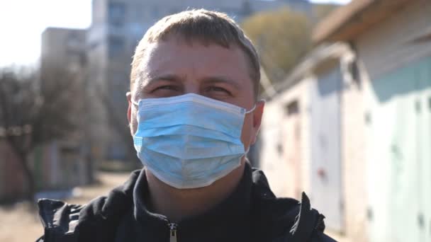 Retrato de homem com máscara facial médica fica na rua da cidade durante a epidemia de COVID-19. Um tipo a usar máscara protectora do vírus ao ar livre. Conceito de saúde e segurança da pandemia de coronavírus — Vídeo de Stock