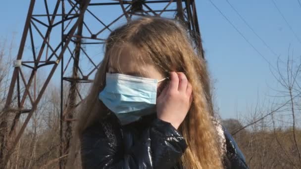 Gelukkig vrouwelijk kind zet beschermende masker van virus COVID-19 en glimlach. Portret van een klein meisje met een medisch gezichtsmasker buiten. Concept van gezondheid en veiligheid van coronaviruspandemie — Stockvideo