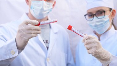 Erkek ve kadın doktorlar koronavirüs için kan örneği içeren test tüpü tutuyorlar. Koruyucu eldivenli ve gözlüklü iki sağlık görevlisi kan örneklerini test ediyor. COVID-19 salgınından sağlık ve güvenlik hayatı kavramı.