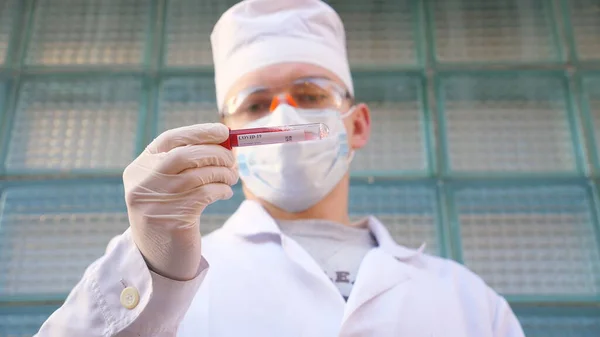 戴防护手套和眼镜的年轻医生在医院检查血液样本 男医生拿着带血样的试管去验尸 Covid 19大流行病的健康和安全寿命概念 — 图库照片