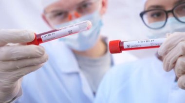 İki doktor koronavirüs için kan örnekleriyle test tüplerini inceliyor. Koruyucu eldivenli erkek ve kadın sağlık görevlileri kan örneklerini test ediyor. COVID-19 salgınından sağlık ve güvenlik hayatı kavramı
