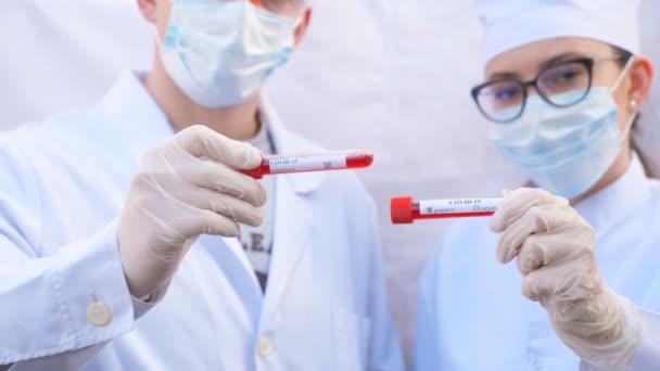 I medici maschili e femminili tengono la provetta con il campione di sangue al coronavirus. Due medici con guanti protettivi e occhiali esaminano campioni di sangue. Concetto di salute e sicurezza da pandemia COVID-19 — Video Stock