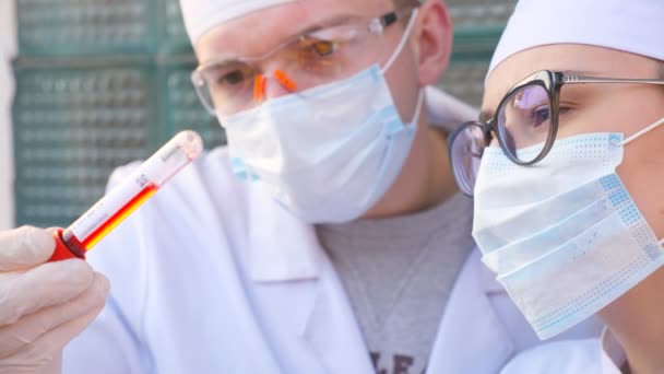 Два лікарі досліджують тестову трубку з кров'яним зразком до коронавірусу. Чоловічі та жіночі ліки з захисними рукавичками перевіряють зразки крові. Концепція здорового і безпечного життя від пандемії COVID-19 — стокове відео