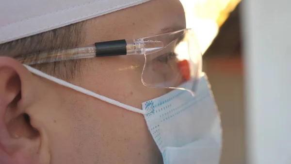 Profile of doctor looking at test tubes with blood samples to coronavirus. Male medic with protective glasses testing blood samples to COVID-19 virus. Concept of health and safety life from pandemic