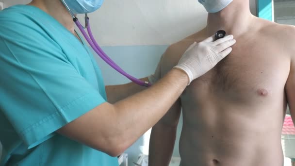 Médico con estetoscopio escucha los pulmones del paciente busca síntomas COVID-19. Doctor examinando al hombre con estetoscopio a los signos de neumonía por coronavirus. Médico revisando el pecho del tipo en el hospital — Vídeo de stock