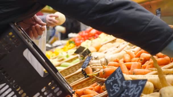 Ręka staruszka wybiera produkty w sklepie spożywczym lub warzywnym. Starszy mężczyzna kupujący z koszykiem wybiera warzywa i wkłada je do plastikowej torby. Różnorodność towarów w supermarkecie. Koncepcja zakupów — Wideo stockowe