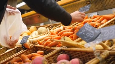 Marketten ya da sebze dükkanından taze havuç seçen bir adamın eli. Erkek alıcı sebze seçiyor ve plastik torbaya koyuyor. Süpermarkette çeşitli ürünler. Alışveriş konsepti. Kapat.