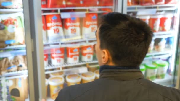 Jongeman die de koelkast opent en ijs of gekoelde boodschappen doet in de supermarkt. Kerel die producten kiest in de supermarkt. Koper bij de levensmiddelenwinkel. Langzame beweging Close-up — Stockvideo