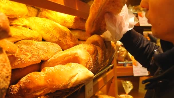 Nahaufnahme eines männlichen Verbrauchers, der frisches Brot aus dem Backregal nimmt und es riecht. Mann wählt Mehlprodukte im Supermarkt aus. Käufer bei der Warenauswahl. Konzept des Einkaufens. Zeitlupe — Stockvideo