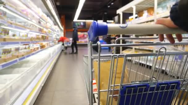 Nerozpoznatelný muž tlačí vozík s výrobky podél řady potravin v supermarketu. Kupující vybírá zboží v obchodě s potravinami. Koncept nakupování. Zpomalený pohyb — Stock video