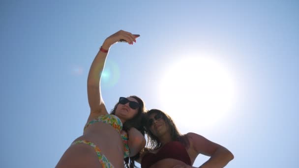 Alegres morenas atractivas tomando retrato selfie en el teléfono inteligente. Mujeres jóvenes y despreocupadas haciendo fotos durante las vacaciones de verano. Damas felices con gafas de sol posando en cámara. Novias descansando juntas — Vídeos de Stock