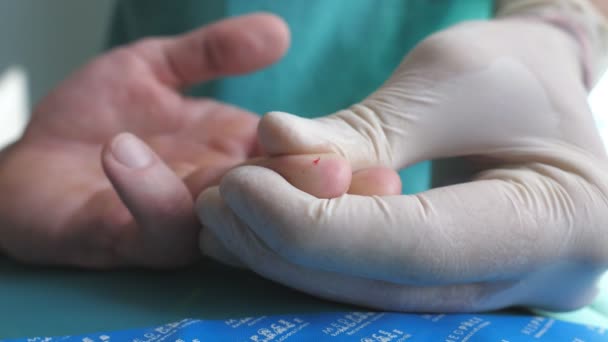 De arts neemt een bloedmonster van de vinger van de patiënt voor test naar COVID-19. Handen van de arts in beschermende handschoenen prikt vinger van de mens met een naald om analyse te nemen om coronavirus tijdens pandemie. Sluiten. — Stockvideo