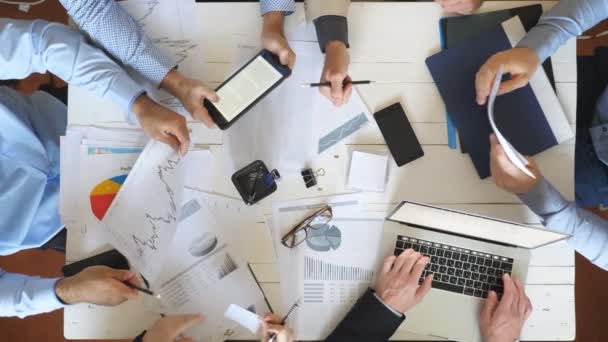 사무실에서 기업 프로젝트에 대한 전략을 계획하는 비즈니스 사람들의 최고보기 남성과 여성의 손. 비즈니스 팀이 테이블에 앉아 재무 그래프를 확인합니다. 책상에서 문서를 검사하는 동료 — 비디오