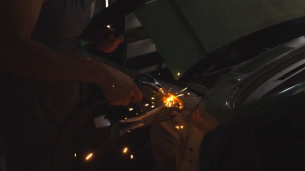 Mano masculina del reparador profesional o del trabajador mecánico suelda las piezas metálicas del coche viejo usando la máquina de soldadura en taller. Los destellos y chispas vuelan desde el trabajo de soldadura en la oscuridad en el garaje. Vista lateral Primer plano — Vídeos de Stock