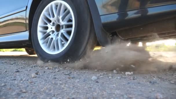 Wheel of car are slip on a asphalt road during start of movement. Small stones and dirt is fly out from under the tire of a auto. Vehicle quickly beginning motion. Concept of burnout. Slow motion — Stock Video