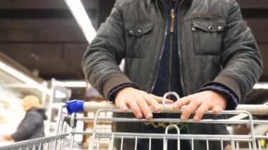 Süpermarkette alışveriş arabasıyla yürüyen tanınmayan bir adam. Alışveriş arabalarını market raflarıyla sırayla iten ve ürün seçen bir adam. Dükkandan bir alıcı. Yavaş çekim. Yakın çekim.