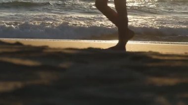 Genç kadın bacakları kuma basıyor. Sahilde altın kumda yürürken arka planda okyanus dalgaları olan kadın ayaklarına yakın dur. Deniz kıyısındaki çıplak ayaklı kız. Yaz tatili. Yavaş çekim