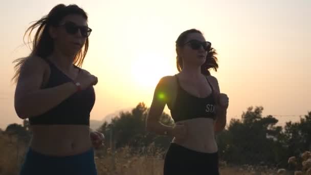 Zwei sportliche Frauen joggen abends über die Landstraße. Junge Mädchen trainieren abends. Sportlerinnen beim Lauftraining im Freien. Konzept eines gesunden aktiven Lebensstils. Zeitlupe — Stockvideo