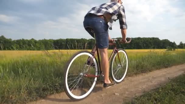若い男が畑の上の田舎道でヴィンテージ自転車に乗っている。田舎のトレイルアウトドアに沿ってスポーティ男サイクリング。田舎で自転車に乗る男性サイクリスト。健康的なアクティブなライフスタイルスローモーション — ストック動画