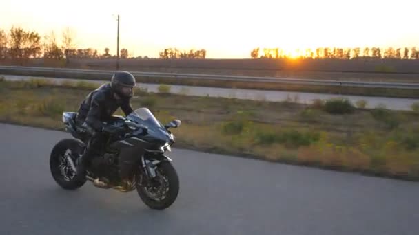 オートバイ愛好家は秋の田舎道で彼のオートバイをレースします。ヘルメットの男は、バックグラウンドで太陽フレアを持つ高速道路で現代のスポーツバイクに乗っています。旅行中にバイクを運転する男。自由の概念 — ストック動画