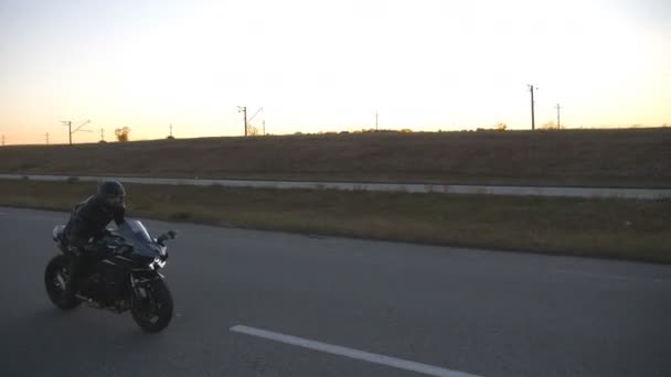 傍晚公路上，戴着头盔的男子骑着现代摩托车。摩托车手在乡间暮色的道路上驾驶摩托车.旅行时骑自行车的家伙。自由和冒险的概念。顶部视图 — 图库视频影像