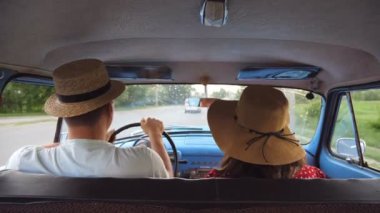 Yolculuk sırasında klasik arabada gezen şapkalı genç bir çift. Tanımlanamayan adam ve kadın eski bir arabanın ön koltuğunda oturuyorlar. Seyahat konsepti. Yavaş çekim Arka plan Görünümü Kapat