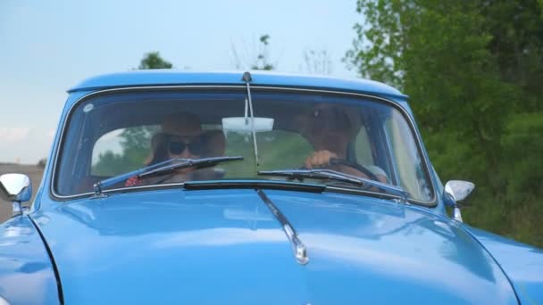 Młoda para w kapeluszach jeżdżąca w zabytkowym samochodzie podczas letnich podróży. Mężczyzna i kobieta siedzą na przednim siedzeniu starego samochodu i rozmawiają podczas jazdy. Koncepcja podróży w wakacje. Powolny ruch Zamknij — Wideo stockowe