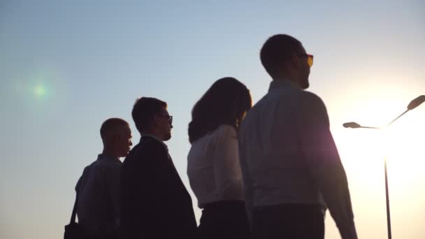 Gruppe junger Geschäftsleute, die bei Sonnenuntergang in der Straße spazieren gehen. Kollegen auf dem Weg nach Hause nach harter Arbeit. Sonnenaufgang im Hintergrund. Erfolgskonzept. Zeitlupe Nahaufnahme Rückansicht — Stockvideo