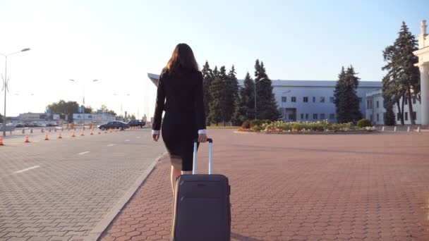 Unerkennbare Geschäftsfrau mit Koffer läuft zum Flughafen, um auf Geschäftsreise zu gehen. Dame in Stöckelschuhen schreitet mit ihrem Gepäck die Straße entlang. Reisekonzept. Rückseite Zeitlupe Nahaufnahme — Stockvideo